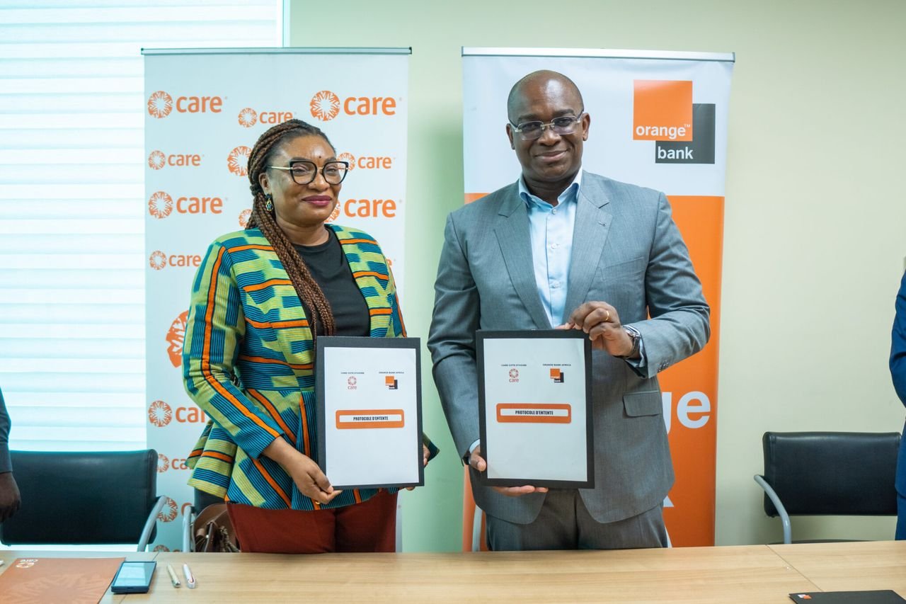 Deux représentants d’Orange Bank Africa et de CARE Côte d’Ivoire présentent le document de partenariat signé devant les bannières des deux organisations.